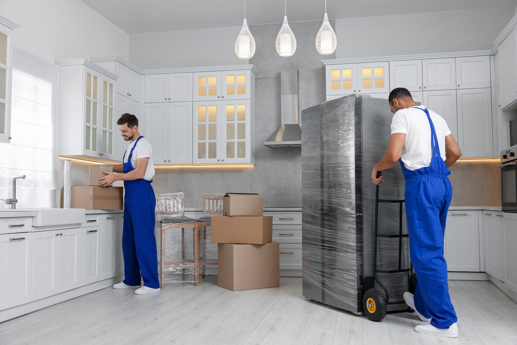 Movers with cardboard boxes and refrigerator in new house