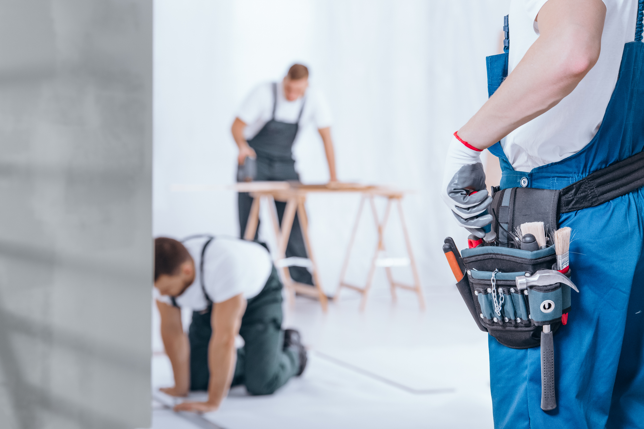 Close-up of handyman with glove on hand and tool belt on blue trousers during home renovation